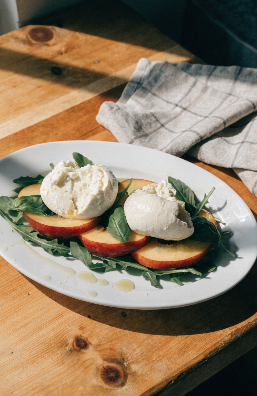 Peach burrata salad on a white platter with arugula, torn burrata, sliced peaches, basil, and balsamic drizzle